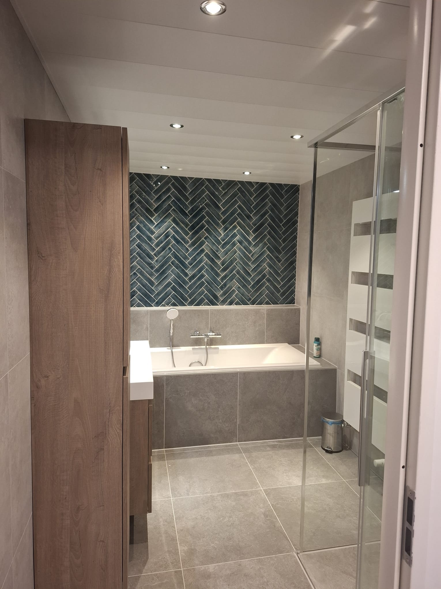 Badkamer met blauwgroene visgraattegels, ligbad en inloopdouche