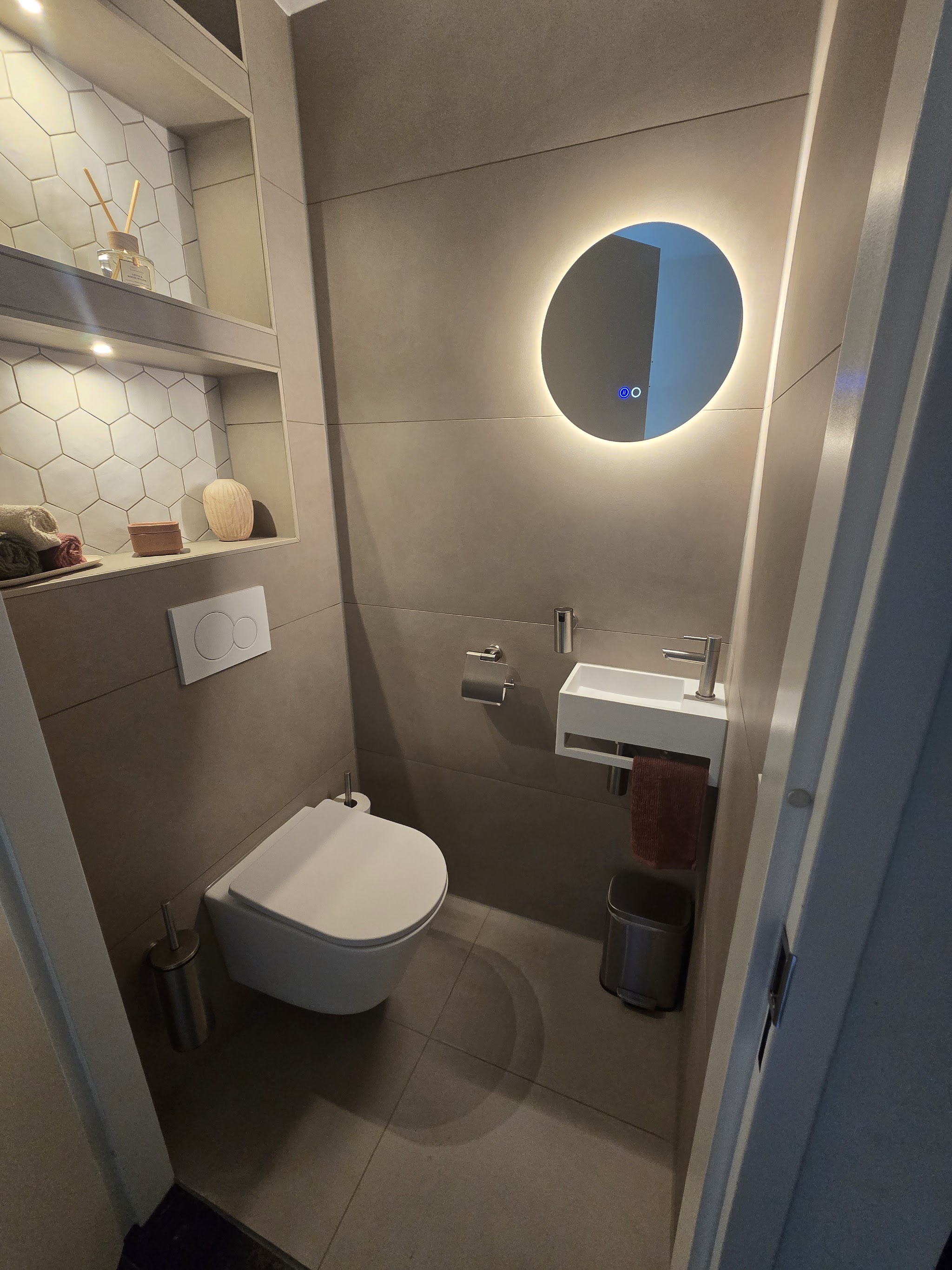 Toilet met hangend closet, rond verlicht spiegel en nis met zeshoekige tegels