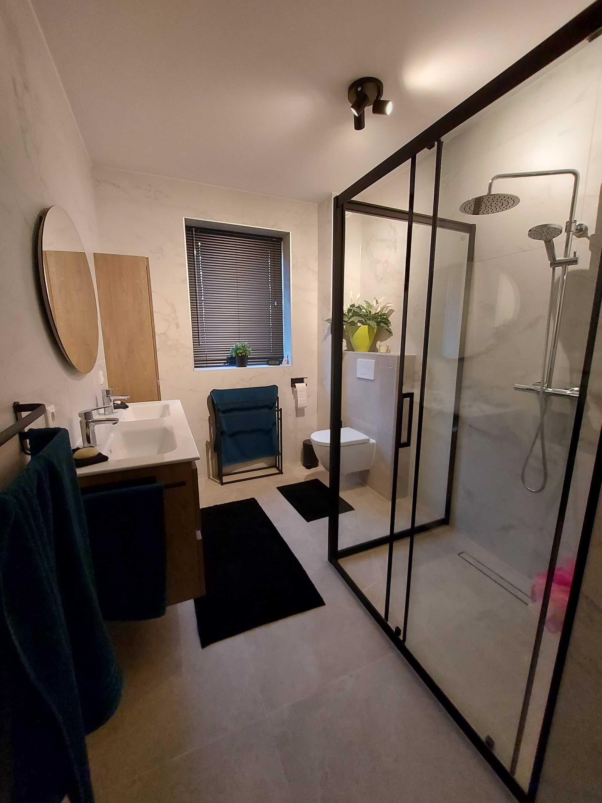 Lichte badkamer met zwart omlijste douchewand en houten badmeubel